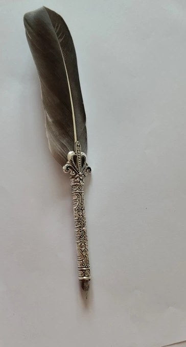 Harmaa sulkakynä ja kuvioitu metallivarsi valkoisella paperilla
