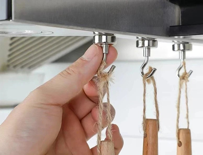 Kolme magneettikoukkua liesituulettimen alapinnassa, koukuissa puisia keittiövälineitä