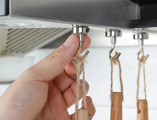 Kolme magneettikoukkua liesituulettimen alapinnassa, koukuissa puisia keittiövälineitä