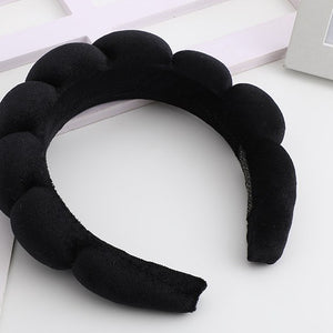 Musta pehmustettu hiusvanne, jonka pinta muodostaa rivin pyöreitä kuplia