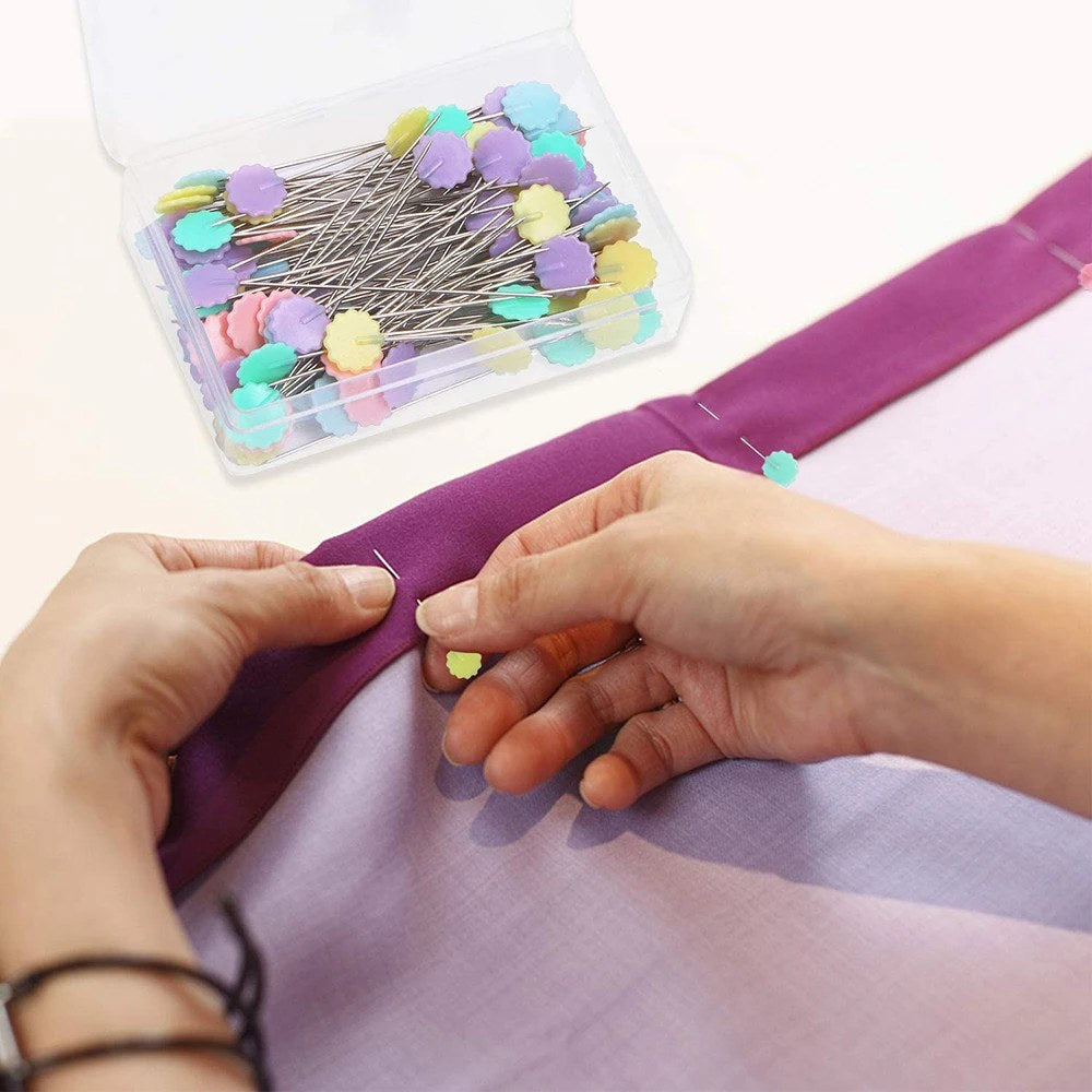 Nuppineulat kukkapäällä kiinnittävät violettia kangasta, avattu rasia taustalla