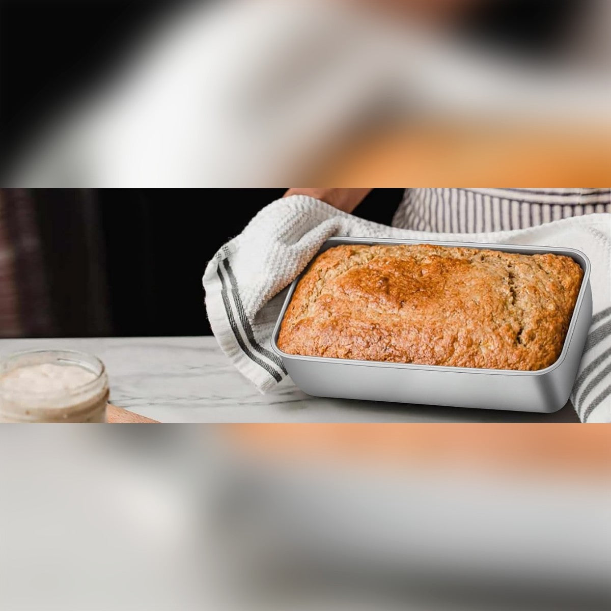 Banaanileipä ruostumattomassa leipävuoassa keittiön tasolla, vieressä keittiöpyyhe