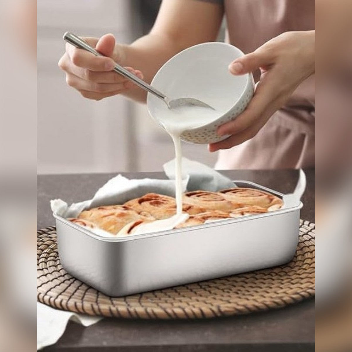 Kuorrutetta kaadetaan leipävuoassa leivinpaperin päällä paistettujen kanelirullien päälle