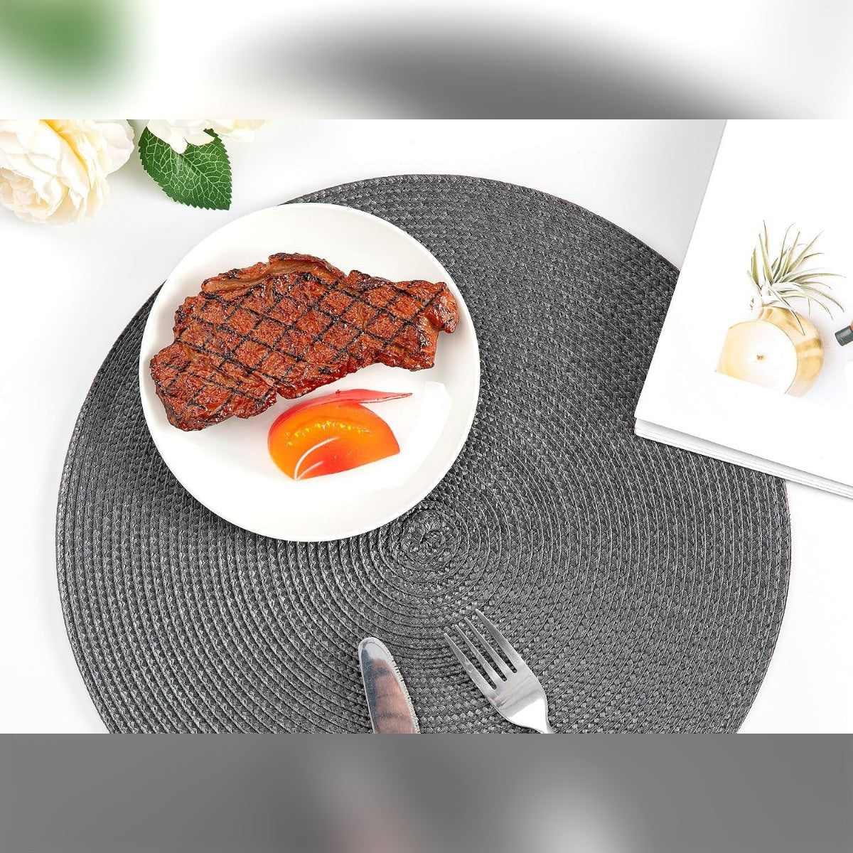 Pyöreä tummanharmaa pöytätabletti, jolla on lautanen, veitsi ja haarukka valkoisella pöydällä