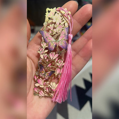 Metallinen kirjanmerkki kädessä: vaaleanpunaiset magnoliat, violetit perhoset ja vaaleanpunainen tupsu (ostajan kuva)