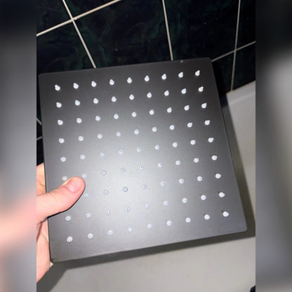 Asiakkaan kuva: 20 cm:n musta neliönmallinen sadesuihkupää kädessä kylpyhuoneessa, valkoiset suuttimet näkyvissä